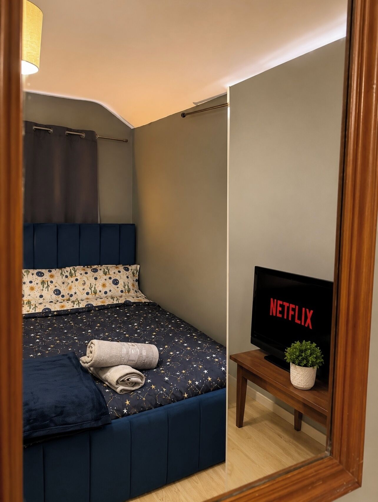 Ein Schlafzimmer mit einem Bett, einem Fernseher, der 'NETFLIX' anzeigt, und einem kleinen Tisch mit einer Pflanze.