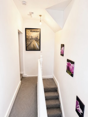 A staircase with a cityscape poster, a light fixture, and two floral paintings. - Cosy room in Wolverhampton perfect for contractors (Wolverhampton)