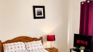 A bedroom with a wooden bed, a bedside table with a lamp, a TV displaying 'NETFLIX,' and a framed photo on the wall. - Cosy room in Wolverhampton perfect for contractors (Wolverhampton)