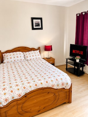A bedroom with a wooden bed, a bedside table with a lamp, a TV displaying 'NETFLIX,' and a framed photo on the wall. - Cosy room in Wolverhampton perfect for contractors (Wolverhampton)