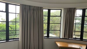 A hotel room with a bed, a desk, and large windows with curtains. - Double Self-Contained Room (Johannesburg)
