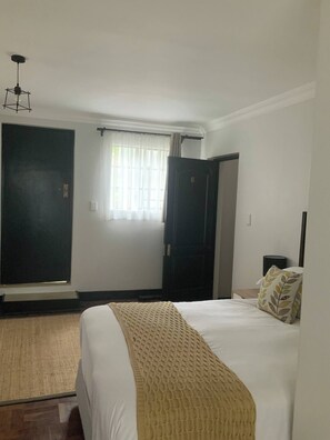 A hotel room with a bed, a window with curtains, a door, and a ceiling fan. - Double Self-Contained Room (Johannesburg)