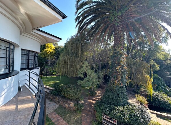 A modern building with a curved balcony, a palm tree, and a well-maintained garden with various shrubs and a pathway. - Double Self-Contained Room (Johannesburg)