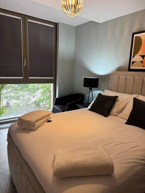 Ein Hotelzimmer mit einem Bett, einem Nachttisch, einer Lampe und einem Fenster mit Jalousien.