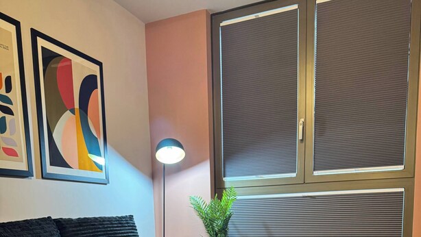 A modern living room with a sectional sofa, a small table, and a large window with blinds. - Apartment in Botanical Gardens, Old Trafford (Stretford, old Trafford)