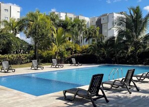 A swimming pool with lounge chairs and palm trees. - Spacious Condo with Pool, Gym, and Central AC in Santiago (Santiago de los Caballeros)