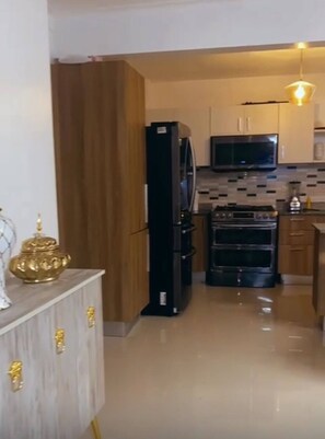 A kitchen with wooden cabinets, a black refrigerator, a microwave, and a stove. - Spacious Condo with Pool, Gym, and Central AC in Santiago (Santiago de los Caballeros)