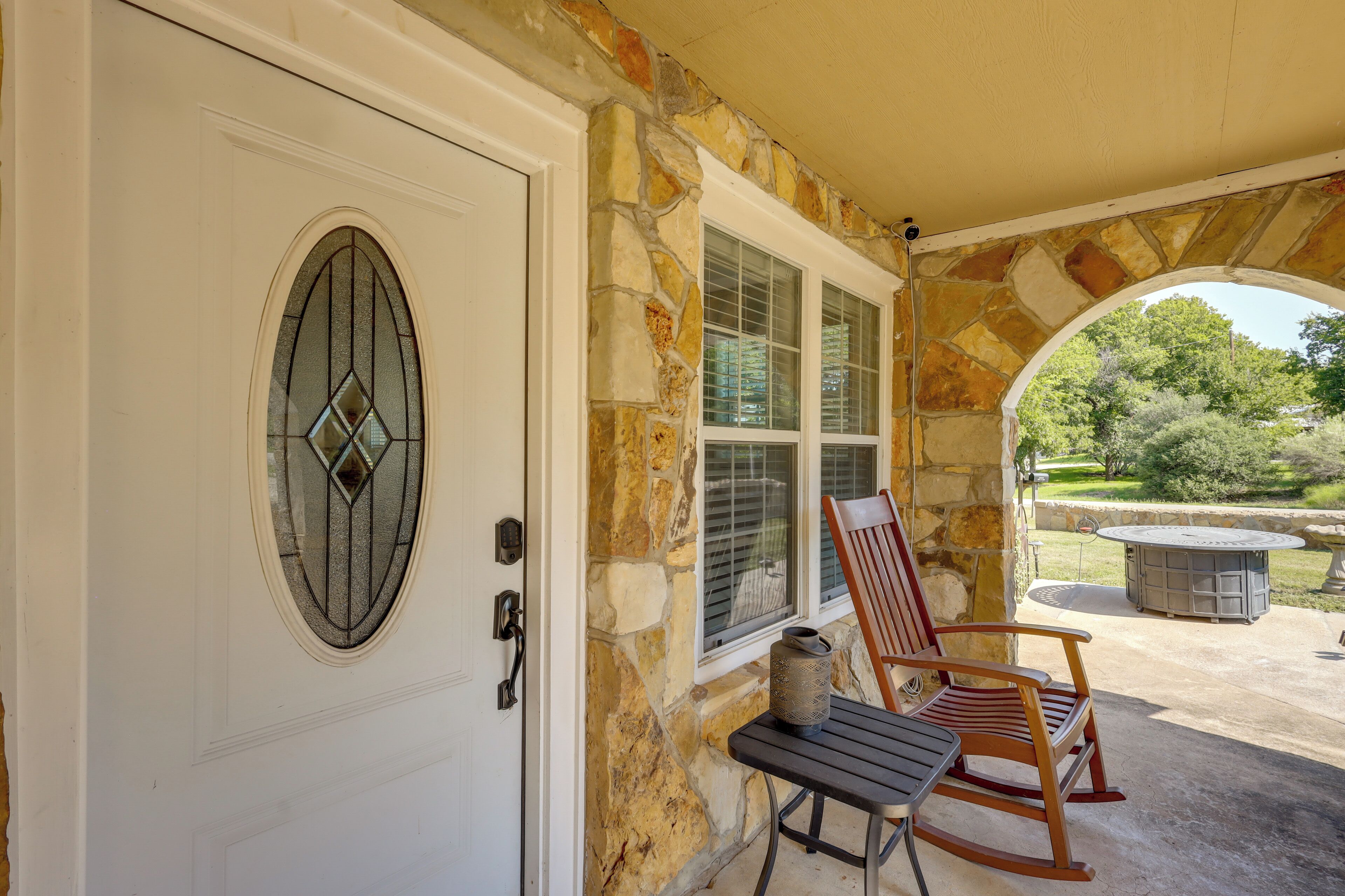 A stone exterior with a white door, a window with shutters, and a patio with a table and two rocking chairs.