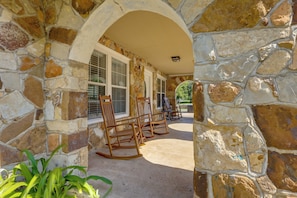 Un arc en pierre mène à un patio couvert, aménagé avec du mobilier d’extérieur et offrant une vue sur le paysage environnant.