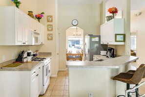 A kitchen with white cabinets, a microwave, a gas stove, and a refrigerator. There is a dining area visible through an archway. - Near Disney & Top Attractions! Poolside Oasis (Davenport)