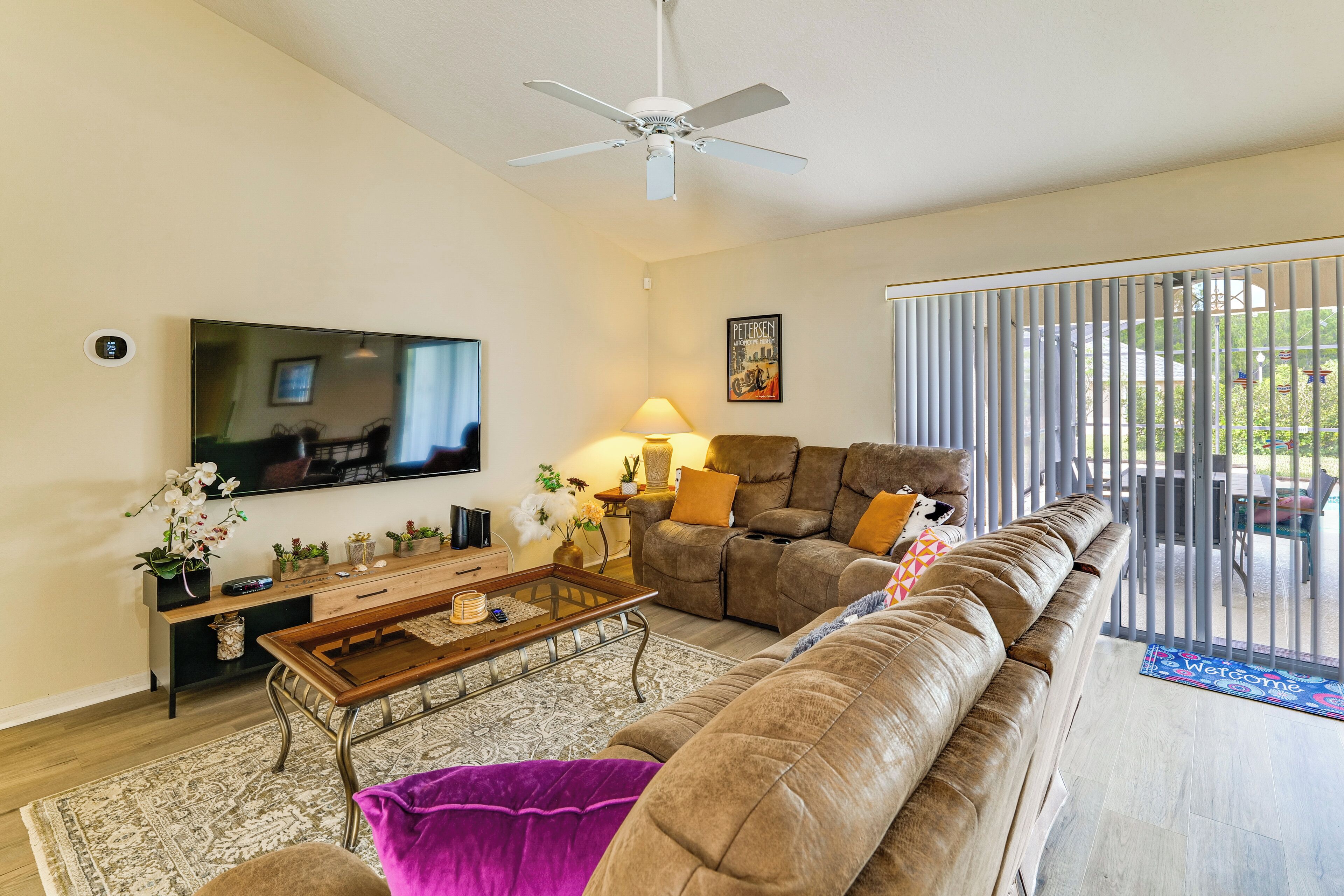A living room with a flat-screen TV, a ceiling fan, a sofa, a coffee table, and a view through a sliding glass door.