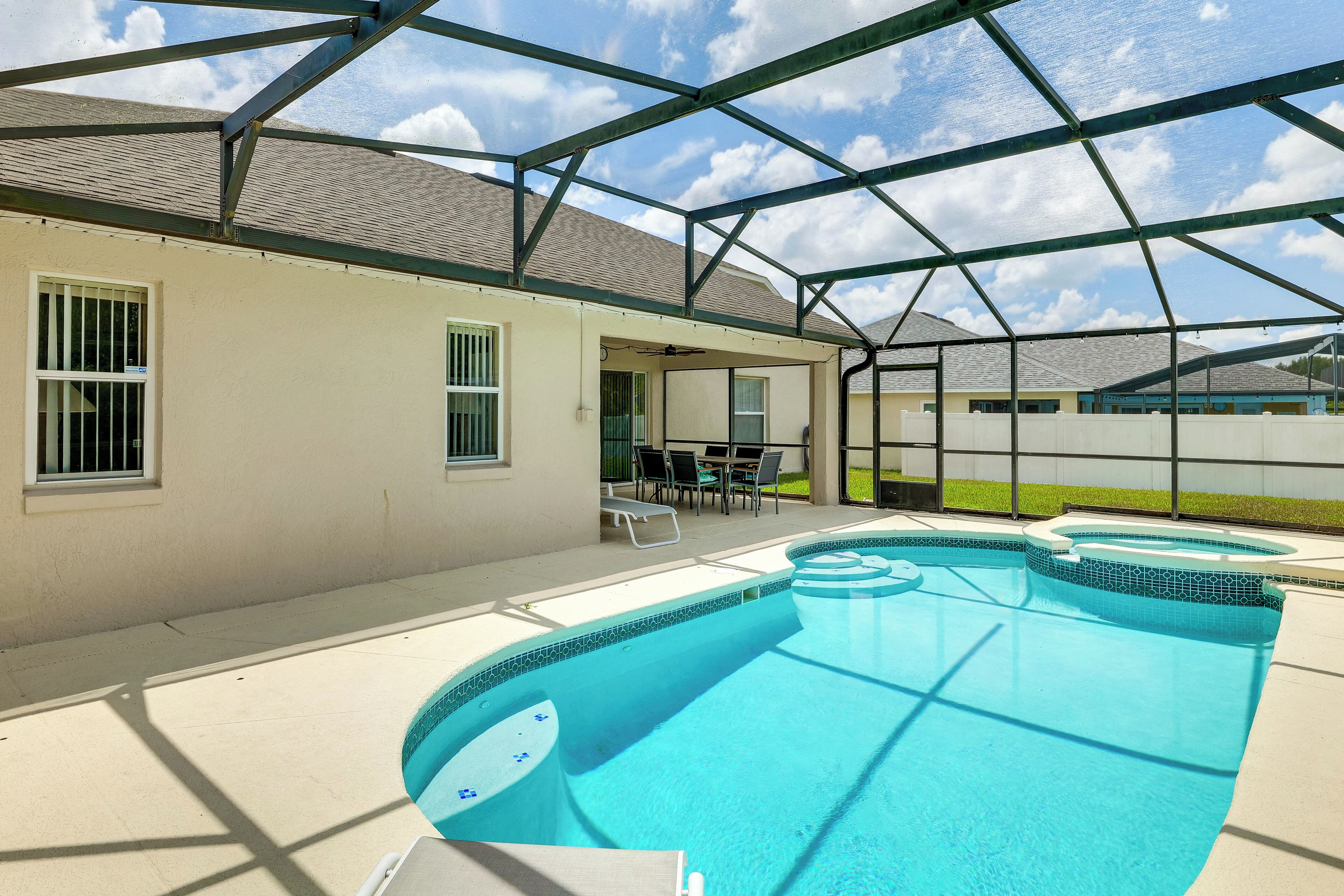 A swimming pool with a covered area, a patio with chairs, and a house with windows.