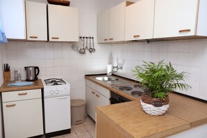 Eine kleine Küche mit weißen Schränken, einem Gasherd, einem Spülbecken und einem Mülleimer.