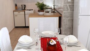 Ruokapöytä on katettu neljälle hengelle: pöydällä on valkoiset lautaset, hopeaesineet ja lasit, punainen pöytäliina ja samppanjapullo.