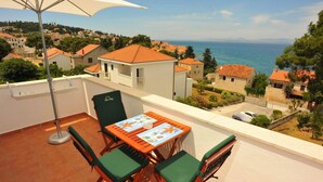 Ein Balkon mit Tisch und Stühlen, mit Blick auf eine Küstenstadt, Häuser und das Meer.