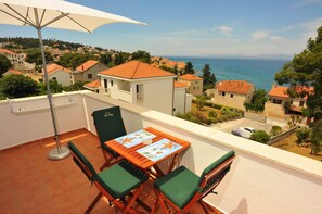 Ein Balkon mit Tisch und Stühlen, mit Blick auf eine Küstenstadt, Häuser und das Meer.