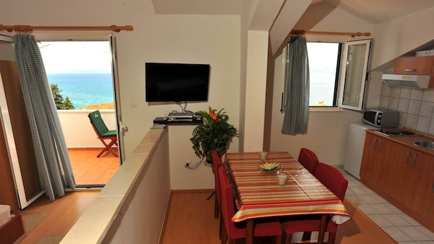 Ein Essbereich mit Tisch, Stühlen, einem Fernseher und Meerblick durch eine Balkontür.