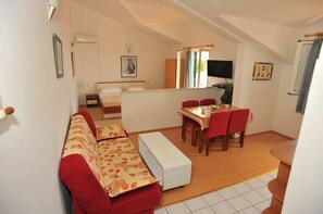 A compact room with a sofa, a small dining table with chairs, a bed, and a television.