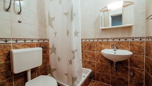 A bathroom with a toilet, a shower with a star-patterned curtain, a sink, and a mirror above the sink. - Studio Apartment (Baska Voda)
