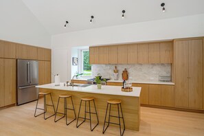 A modern kitchen with wooden cabinets, a stainless steel refrigerator, a large island with stools, and pendant lighting. - Catskills New Build w/ Private Hot Tub & Fire Pit! (Cairo)