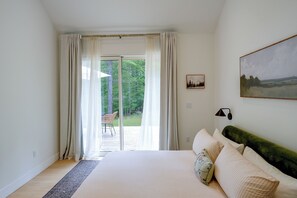 A bedroom with a large bed, a view of a forest through a sliding glass door, and a painting on the wall. - Catskills New Build w/ Private Hot Tub & Fire Pit! (Cairo)
