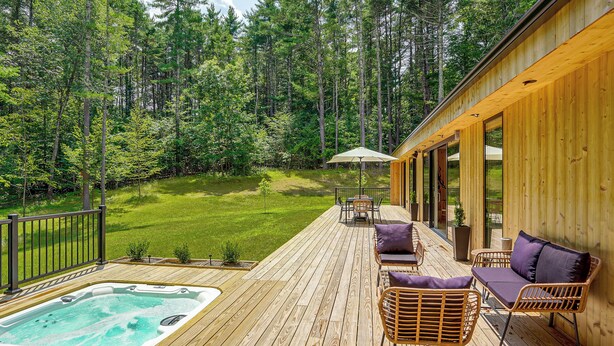Una terraza de madera con jacuzzi, mobiliario exterior y vistas a un bosque.