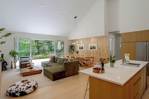 A modern open-plan living and dining area with a large window, wooden flooring, and a central island with a sink.