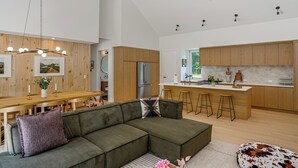 Cocina moderna con armarios de madera, refrigerador de acero inoxidable y una barra con taburetes.