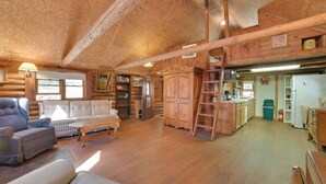 Interior de una cabaña de madera con sala de estar, cocina y habitación en el altillo.