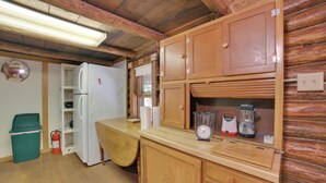Interior de una cabaña de madera con refrigerador, armarios de madera, mostrador de madera y un bote de basura verde.