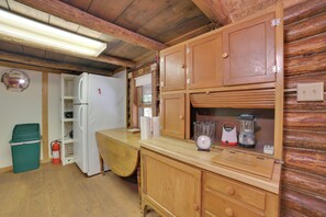 Ein Interieur einer Holzhütte mit einem Kühlschrank, Holzschränken, einer Holzauszug und einer grünen Mülltonne.