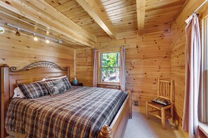 A wooden cabin bedroom with a bed, a nightstand, a chair, and a window with curtains. - Incredible Views! Log Cabin w/ Wraparound Deck (Angel Fire)
