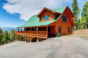 A two-story log cabin with a green roof, a porch, and a view of mountains. - Incredible Views! Log Cabin w/ Wraparound Deck (Angel Fire)