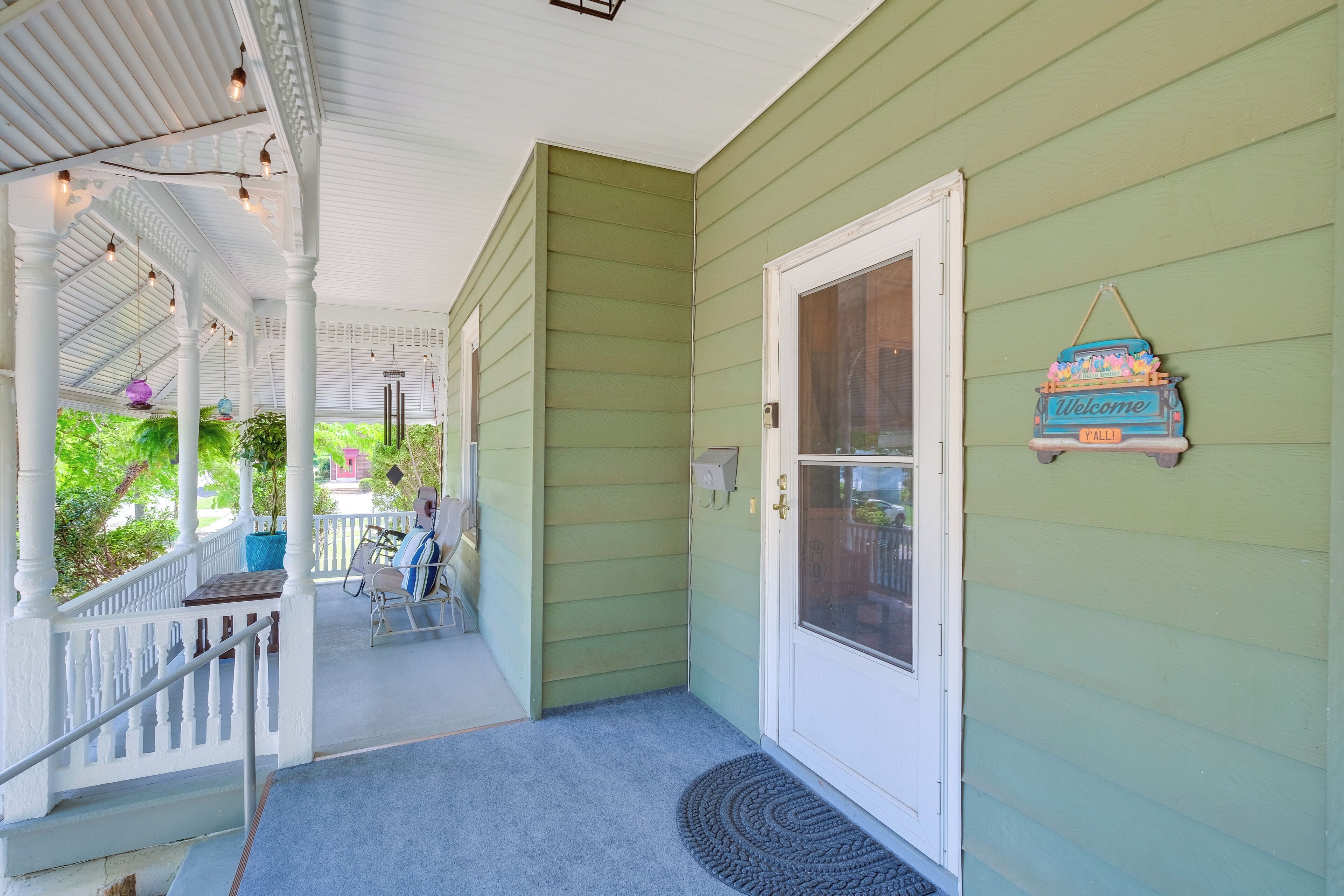 Un porche avec une balustrade blanche, une pancarte de bienvenue et une porte dotée d’un panneau en verre.
