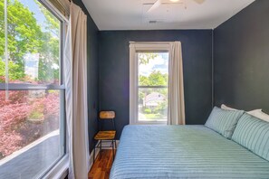 A bedroom with a large window, a bed with striped bedding, and a small wooden chair. - 2 Lynchburg Units: Mansfield Manor & King's Suite! (Lynchburg)