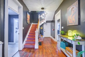 A hallway with a wooden staircase, a desk with plants, and a painting on the wall. - 2 Lynchburg Units: Mansfield Manor & King's Suite! (Lynchburg)