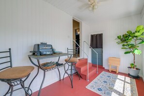 Una habitación compacta con kitchenette, una zona de comedor con dos sillas, una mesita, una planta en maceta y una escalera.