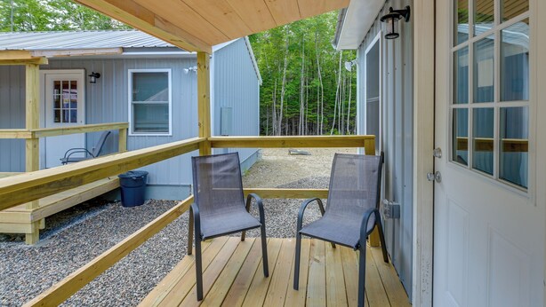 A wooden deck with two chairs, a small table, and a covered area with a window overlooking a forest. - Ride, Fish & Hunt! Downeast Studio on The Airline (Wesley)