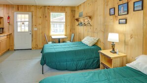 A room with two beds, a small table, a chair, a lamp, and a wall-mounted coat rack. - Ride, Fish & Hunt! Downeast Studio on The Airline (Wesley)