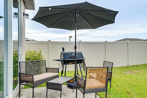 Une terrasse extérieure équipée d’un barbecue, de deux chaises, d’une table et d’un grand parasol.