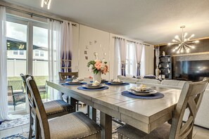 Un coin repas avec une table dressée pour quatre personnes, des chaises, un vase rempli de fleurs et un mur orné de chiffres romains.