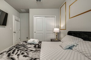 Une chambre à coucher comprenant un lit, une table de chevet avec une lampe, un téléviseur fixé au mur et une porte avec un porte-manteau.