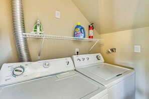 A laundry area with a stacked washer and dryer, a drying rack, and shelves holding cleaning supplies. - Pool Access & Balcony! Colorado Springs Getaway (Colorado Springs)