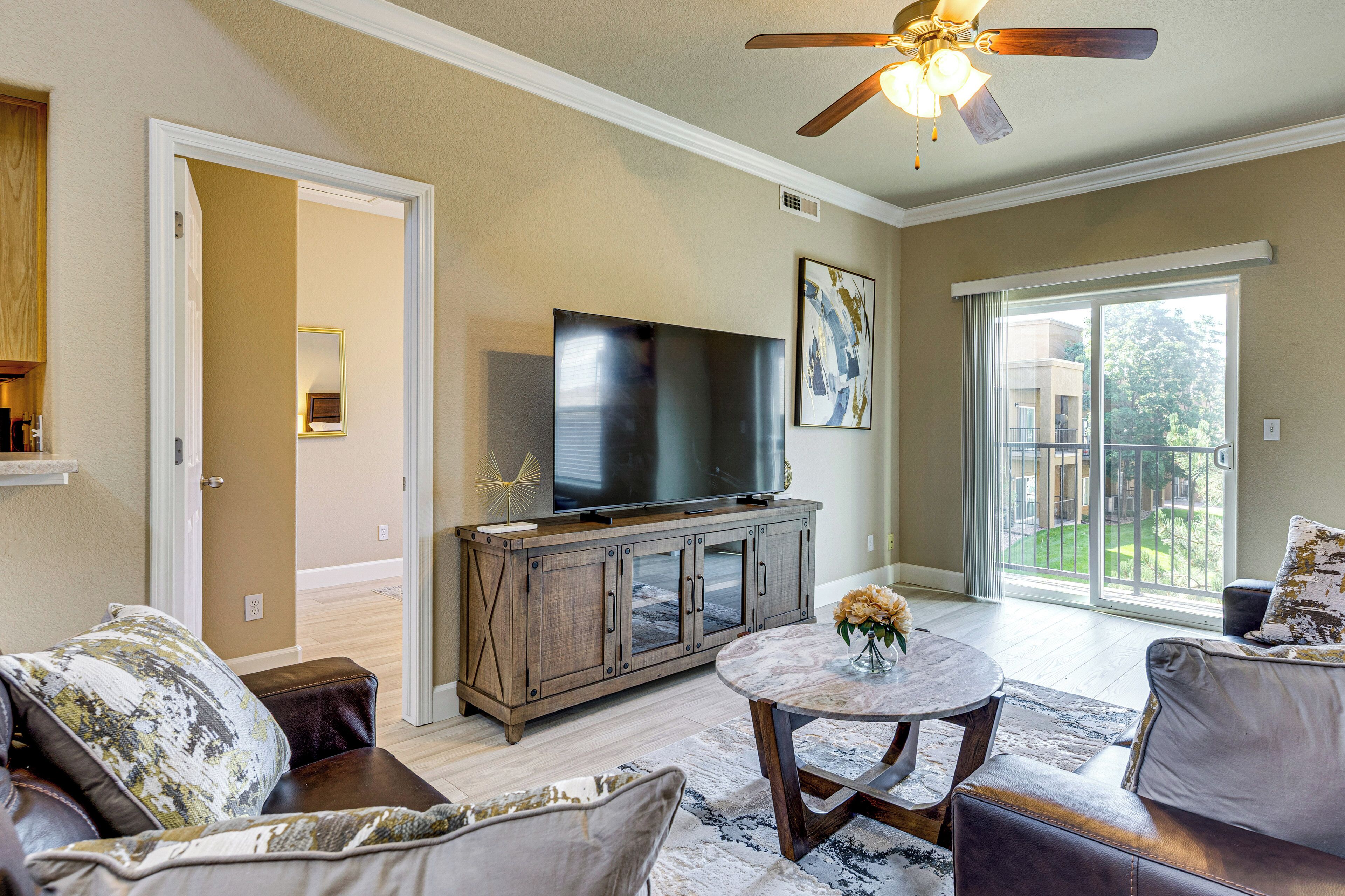 A living room with a television, a ceiling fan, a large window, and a view of the outdoors.
