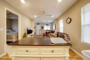 A spacious living area with a kitchen island, a dining table, and a sofa. There is a ceiling fan, a clock, and a window with blinds. - Dual Cottage Escape Walkable to GOTL Strip (Geneva)