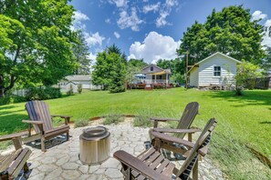Un jardin avec un foyer en pierre, des fauteuils Adirondack en bois et une maison dotée d’un porche.