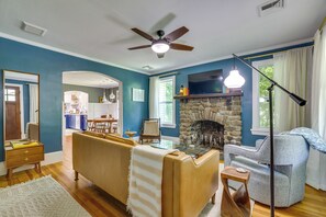 Un salon doté d’une cheminée en pierre, d’un ventilateur de plafond et d’un coin repas visible à travers une arche.