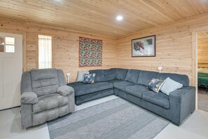 A cozy room with a grey sectional sofa, a grey armchair, and a patterned wall hanging.