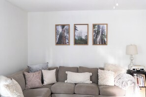 Un salon avec un canapé gris, trois tableaux encadrés représentant des arbres et une lampe sur une table d’appoint.