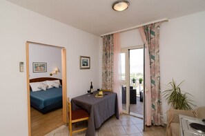 Ein Zimmer mit einem Bett, einem Tisch mit einer Flasche und Gläsern sowie Blick durch eine Tür.